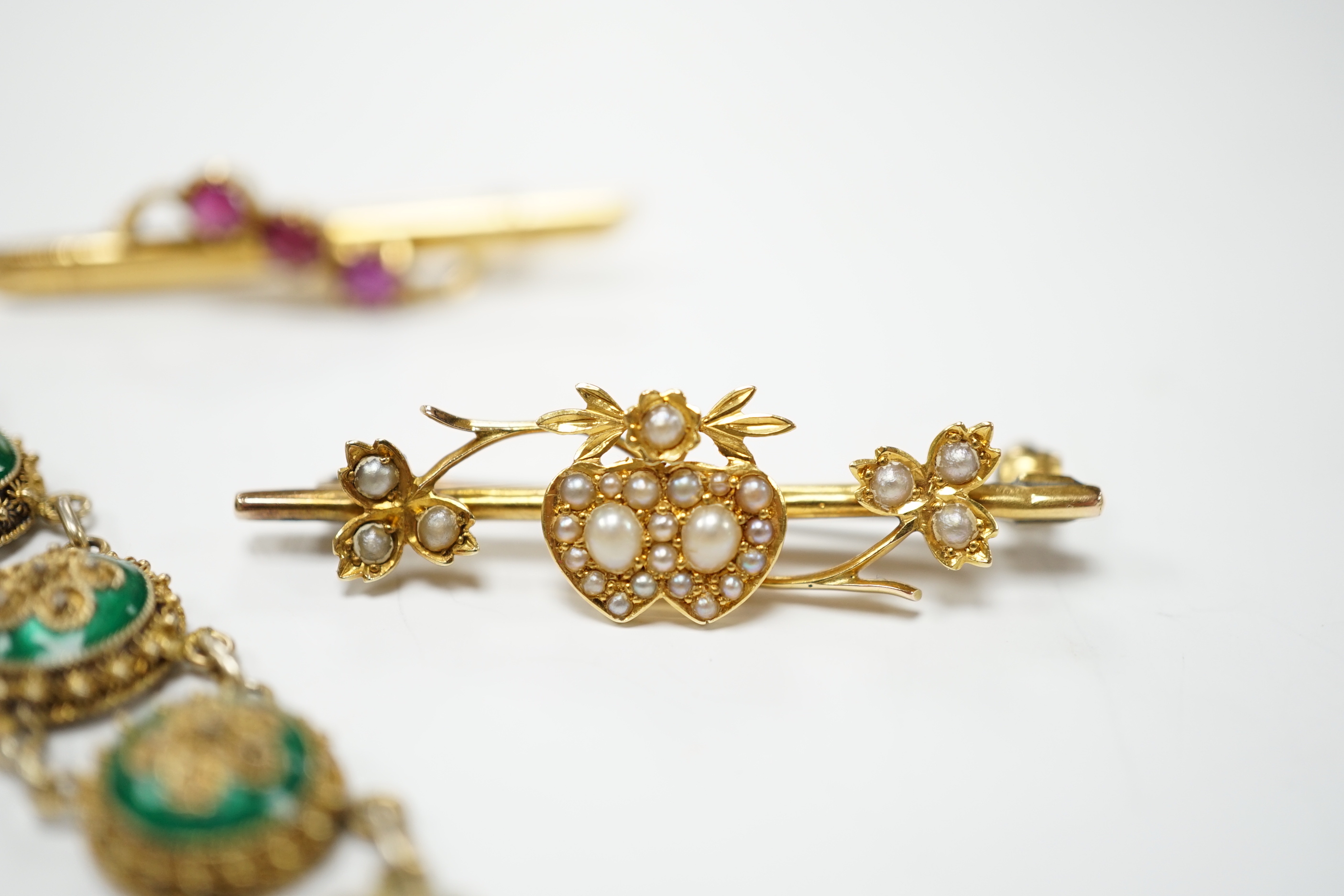 An Edwardian yellow metal, amethyst and split pearl set drop pendant, 52mm, on a yellow metal fine link chain, 45cm, a similar yellow metal and seed pearl set twin hearts bar brooch, a yellow metal and three stone ruby s